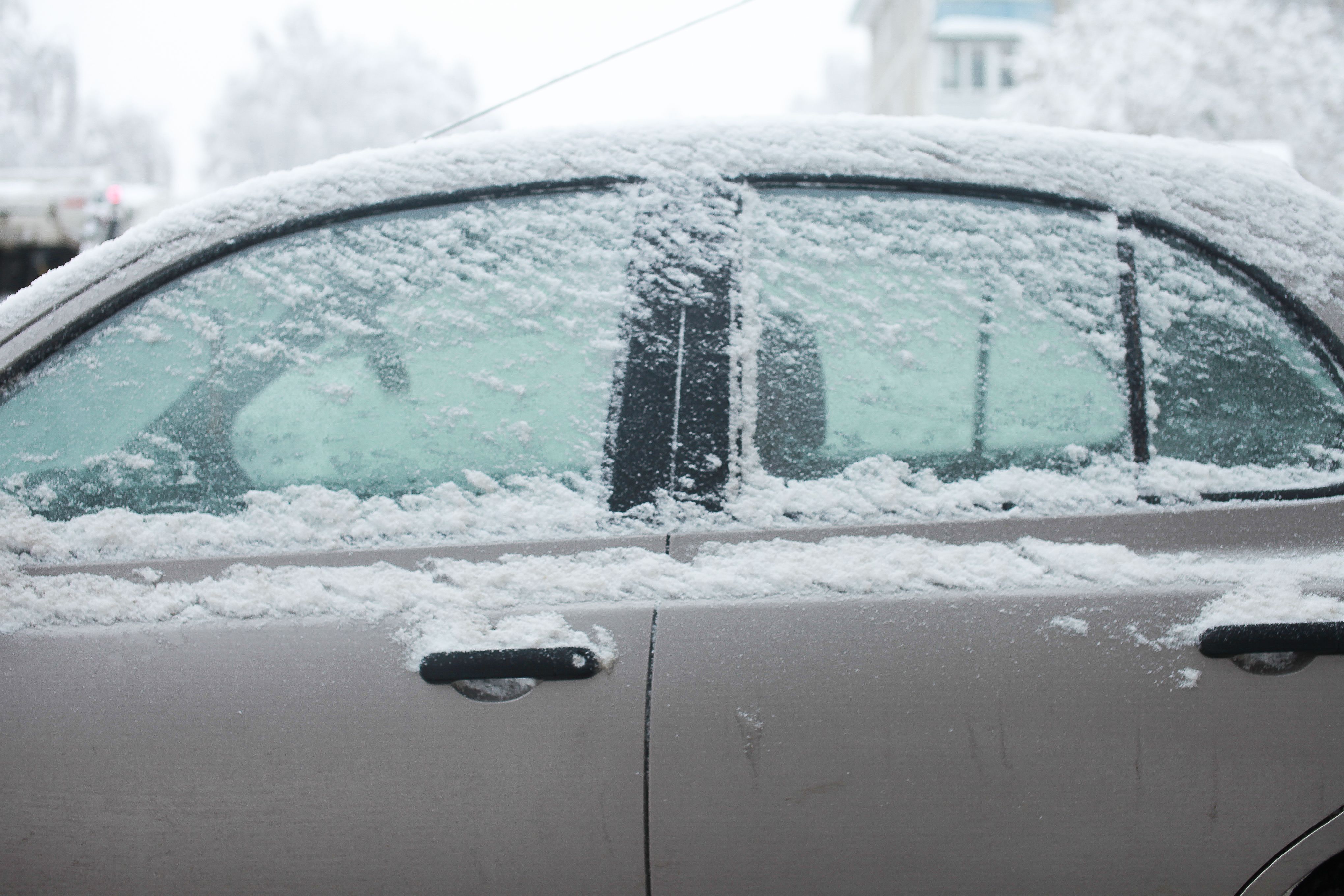 Driver safely removing ice from a frozen car door in winter